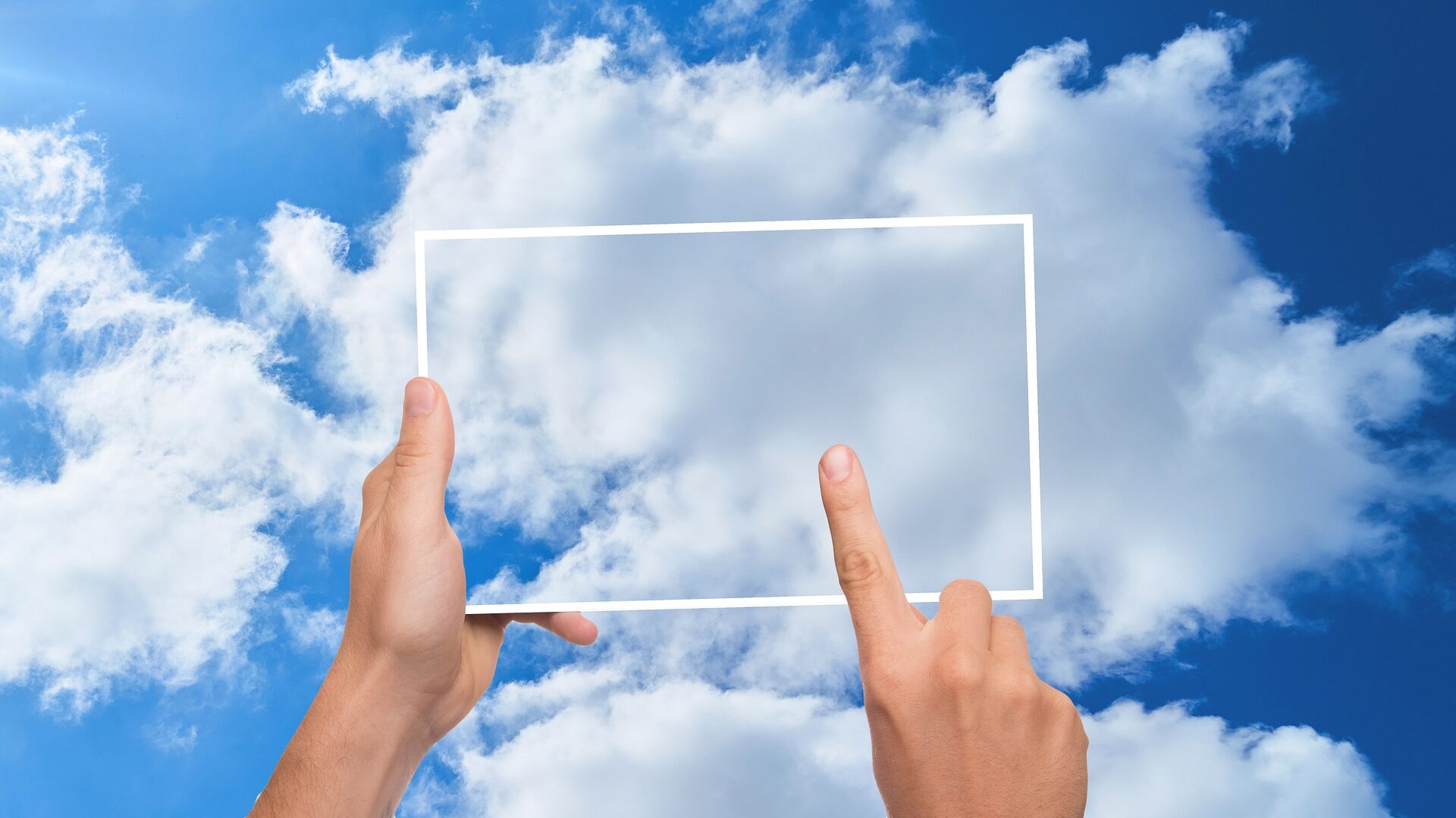 transparentes Tablet vor einer Wolke am blauen Himmel, gehalten von einer Hand, ein Finger tippt darauf
