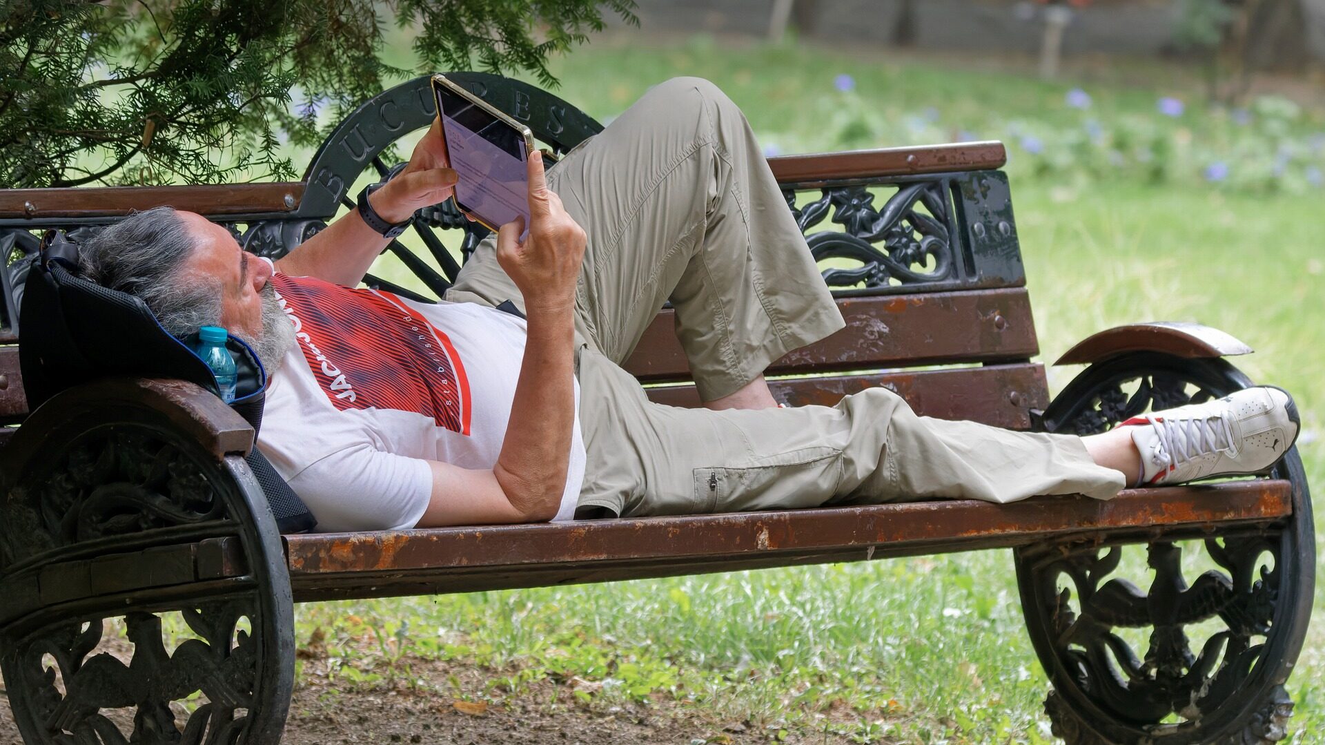 Ein Mann liegt auf einer Bank im Freien und liest auf seinem Outdoor Tablet